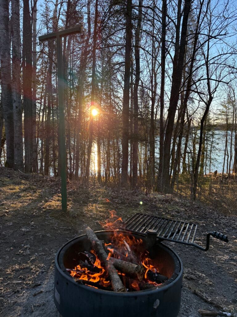 Sunrise through the trees with a campfire and Rainy River in the background